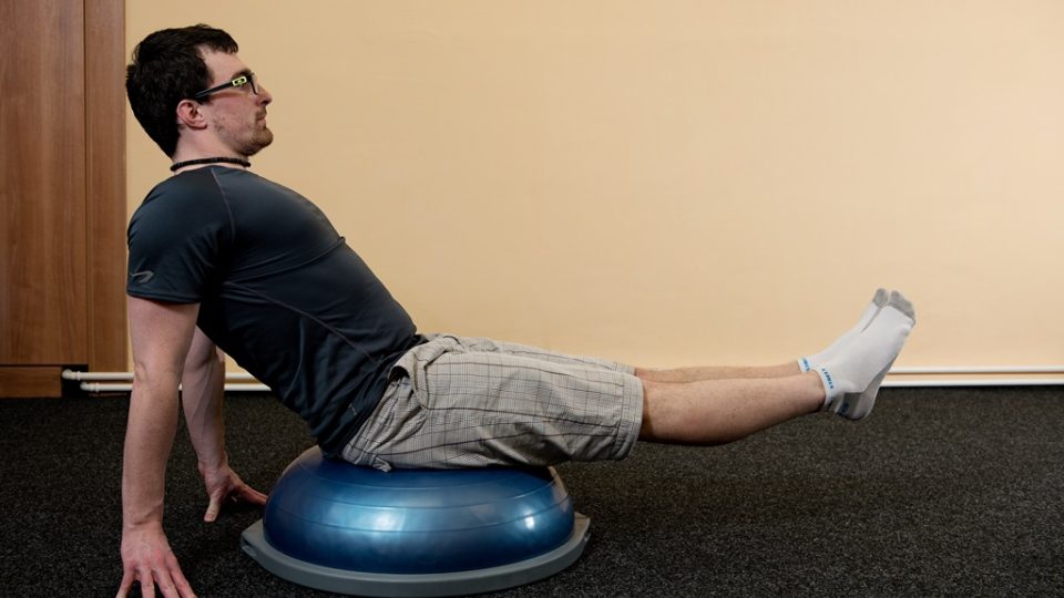 Základní poloha při posilování břicha. Posaďte se na bosu s důkladně rovnými zády a zpevněným břichem. Ruce se opírají o zem a nohy jsou natažené v prostoru