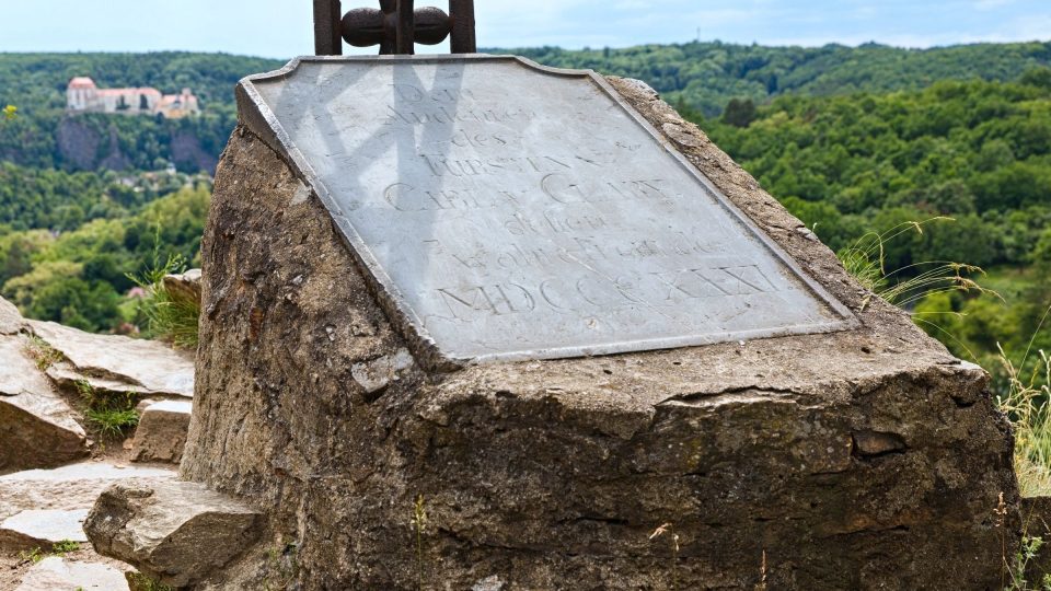 U paty kříže je pamětní deska připomínající malíře, spisovatele a humanistu Carla Claryho. V pozadí je zámek Vranov nad Dyjí